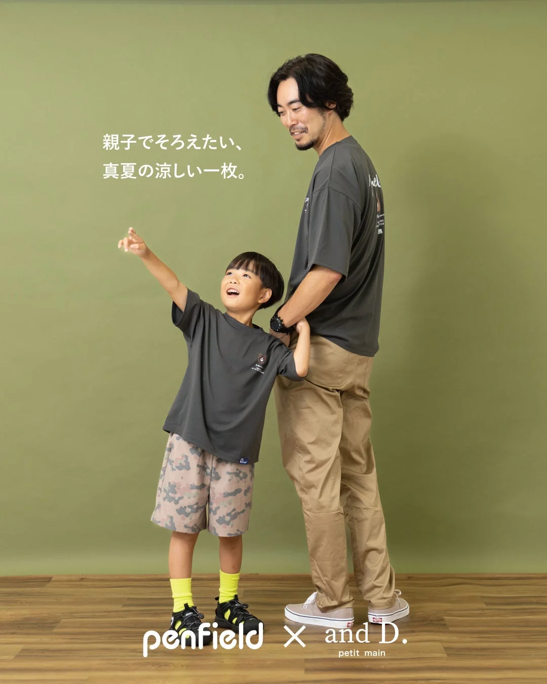 緑の背景の前で、父親と息子が並んで立ち、息子が何かを指差している写真