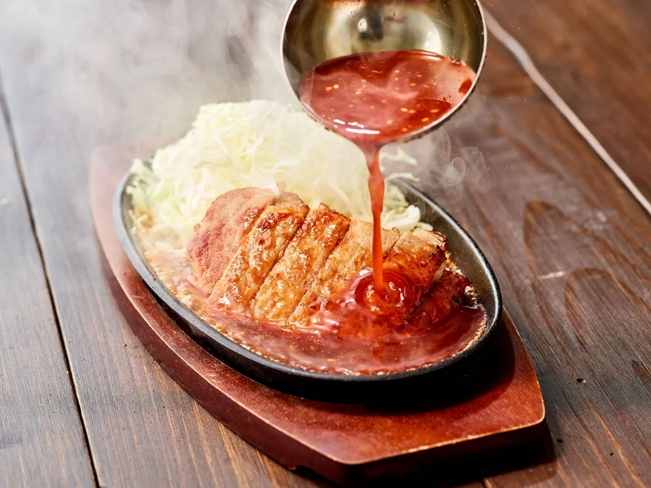 熱々鉄板で特製だれをかける様子