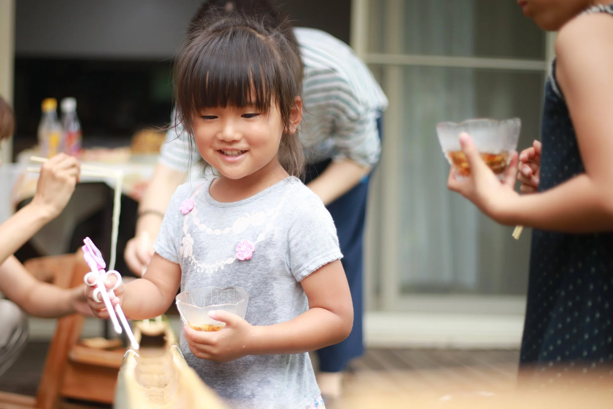 流しそうめんを楽しむ幼い女の子が笑顔を見せている