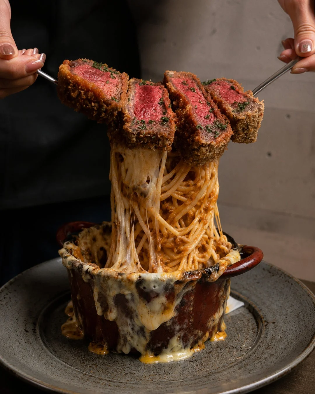 揚げたステーキが乗った濃厚なミートソーススパゲッティが、とろけるチーズと共に持ち上げられている食欲をそそる料理の写真です。豪華でボリューム満点の一皿です。
