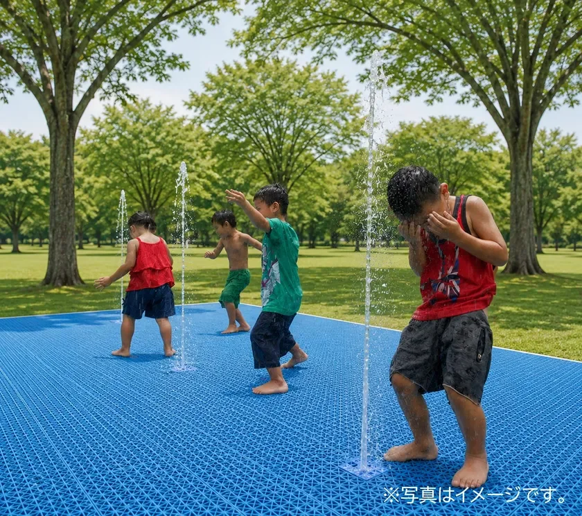 公園の青い水遊び場で、子供たちが噴水の水しぶきを浴びて楽しそうに遊んでいる夏の風景