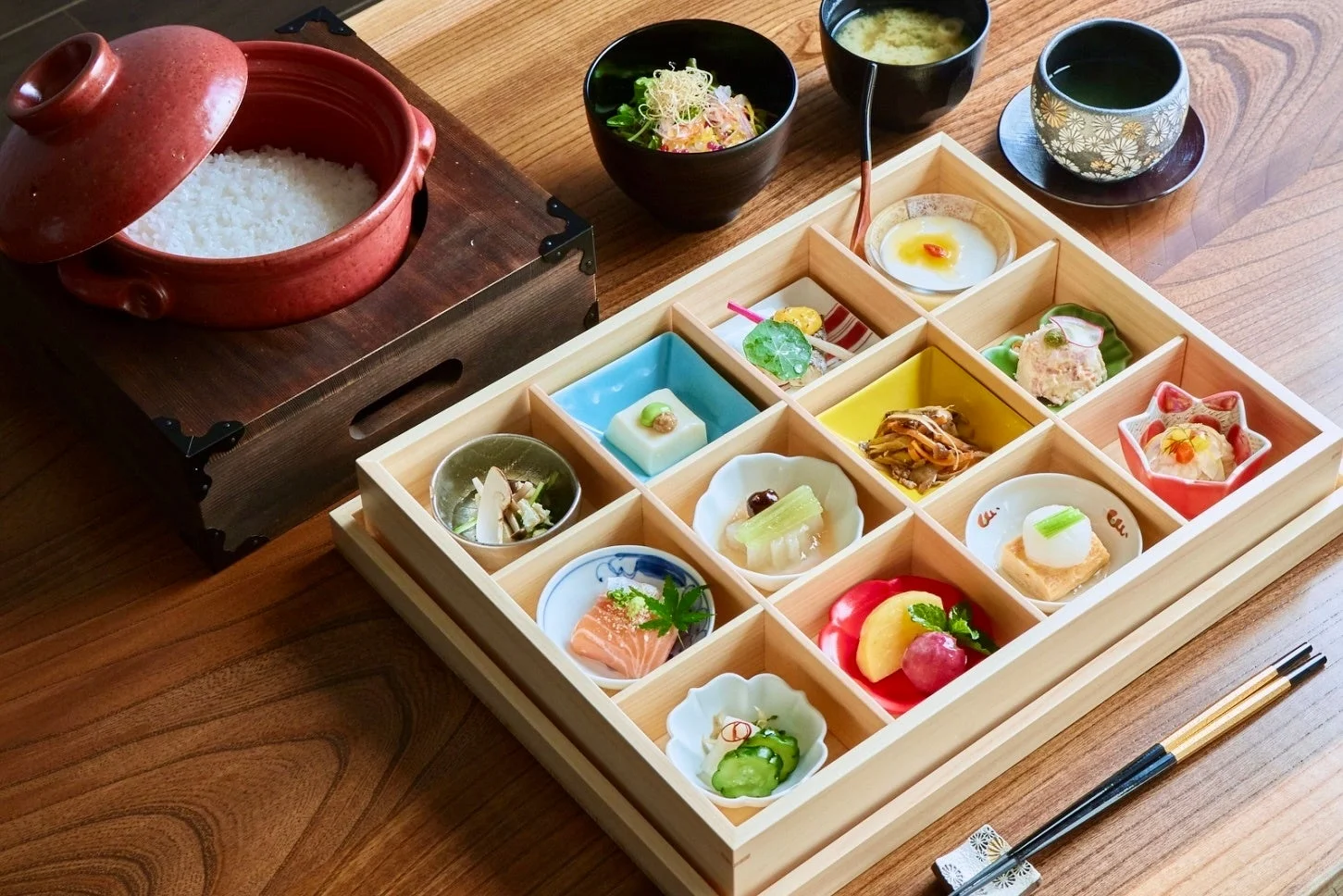 木製の箱に美しく盛り付けられた色とりどりの小鉢料理と、炊きたてのご飯、味噌汁、お茶が並ぶ豪華な和食膳