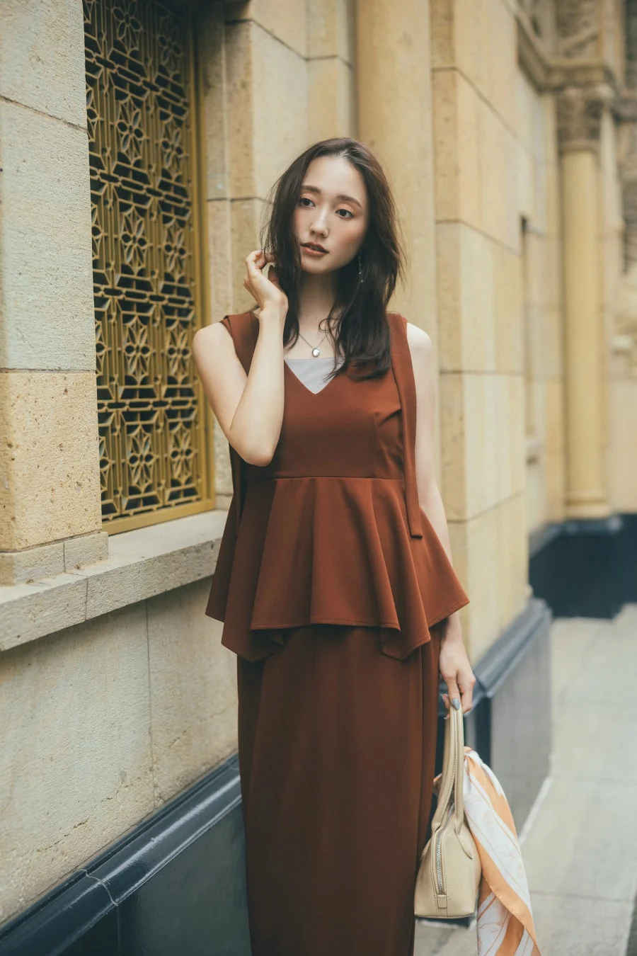 街並みを背景に立つブラウンのセットアップの女性