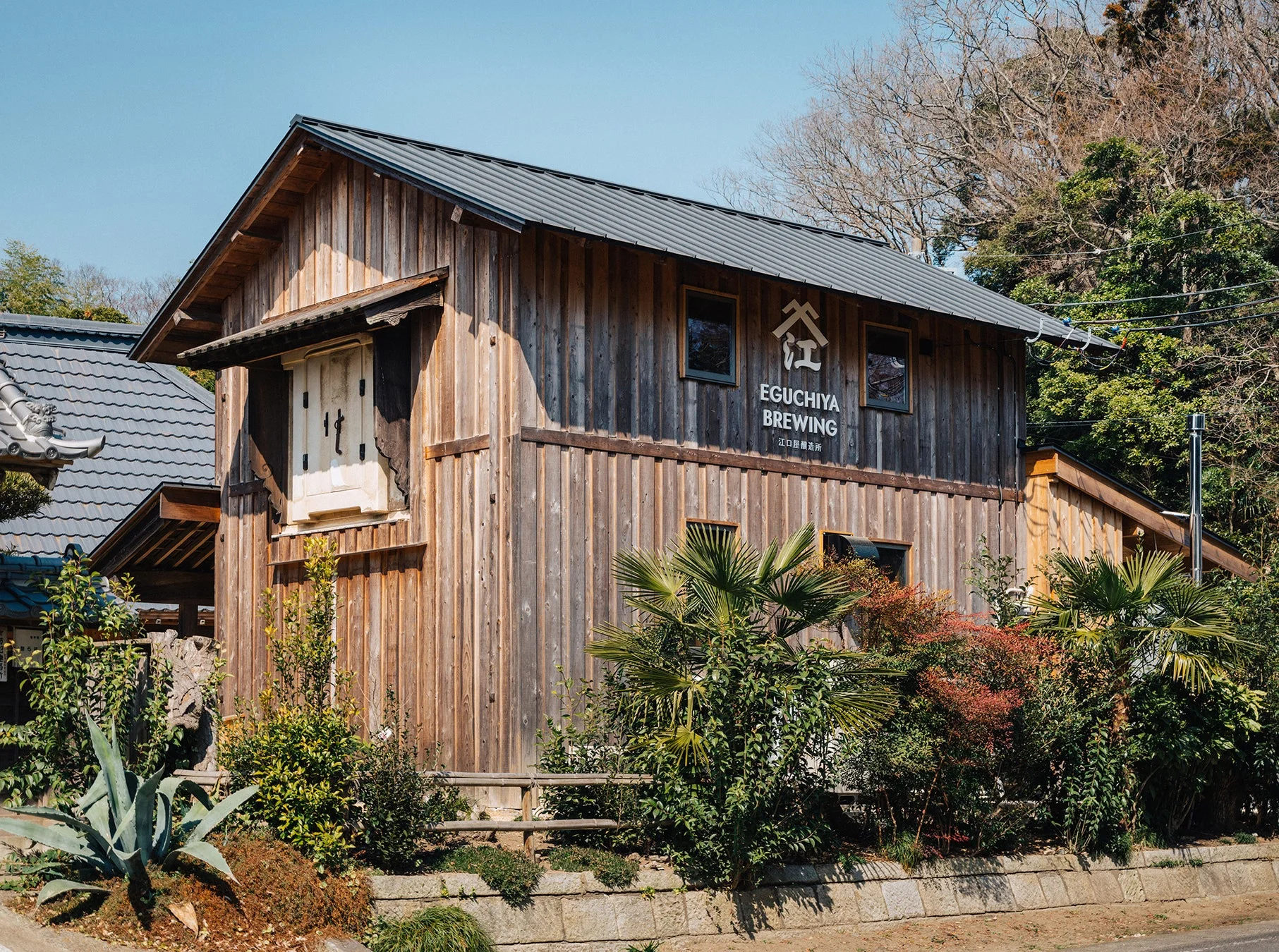 青空の下、木造の趣ある建物が広がる風景。建物には「EGUCHIYA BREWING 江口屋醸造所」の看板がある。