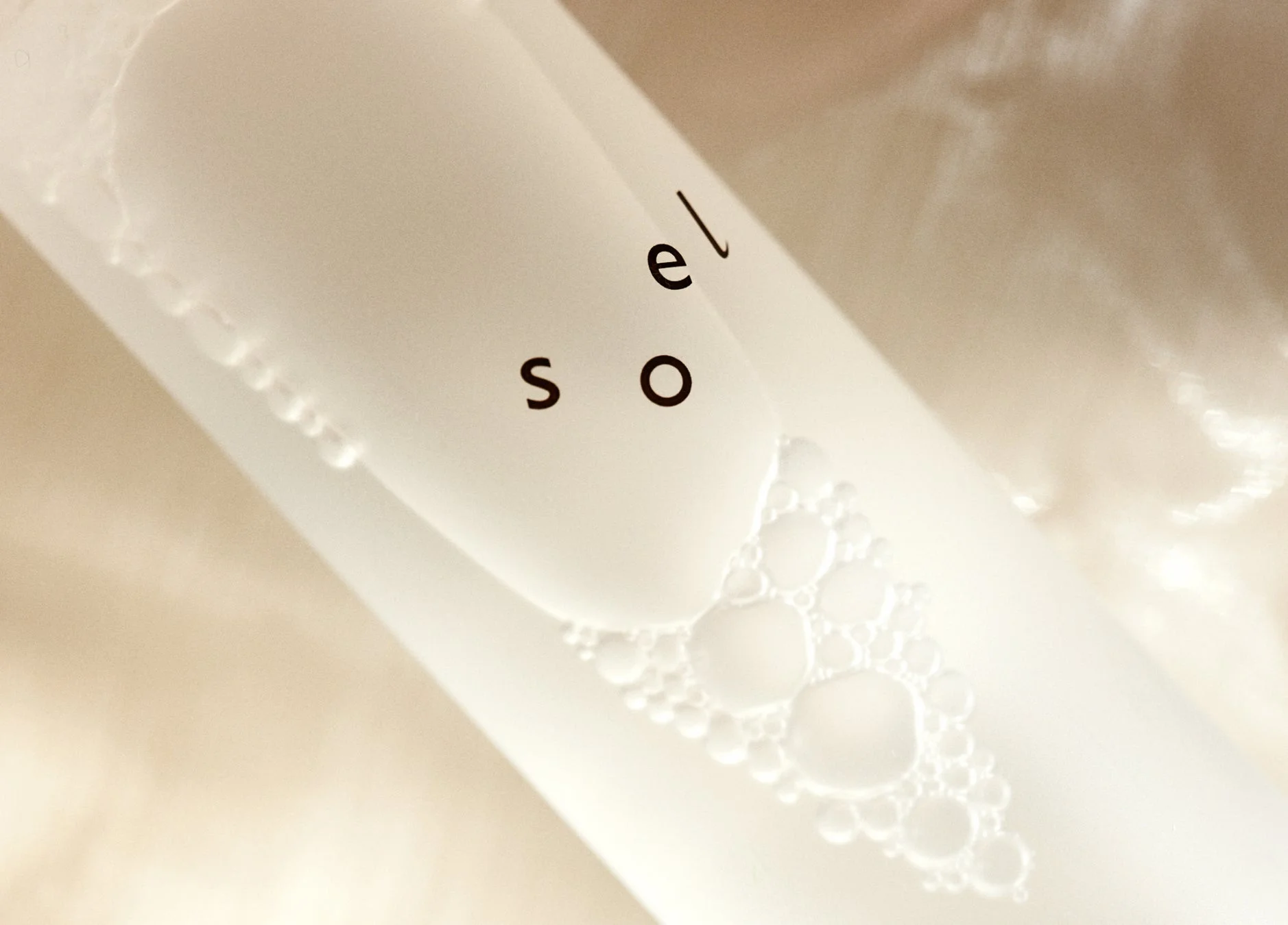 白い容器に入った液体またはジェルのクローズアップ画像です。容器には「so el」の文字と、大小さまざまな泡が見えます。清潔感のある明るいトーンで、美容製品やスキンケア製品を想起させます。