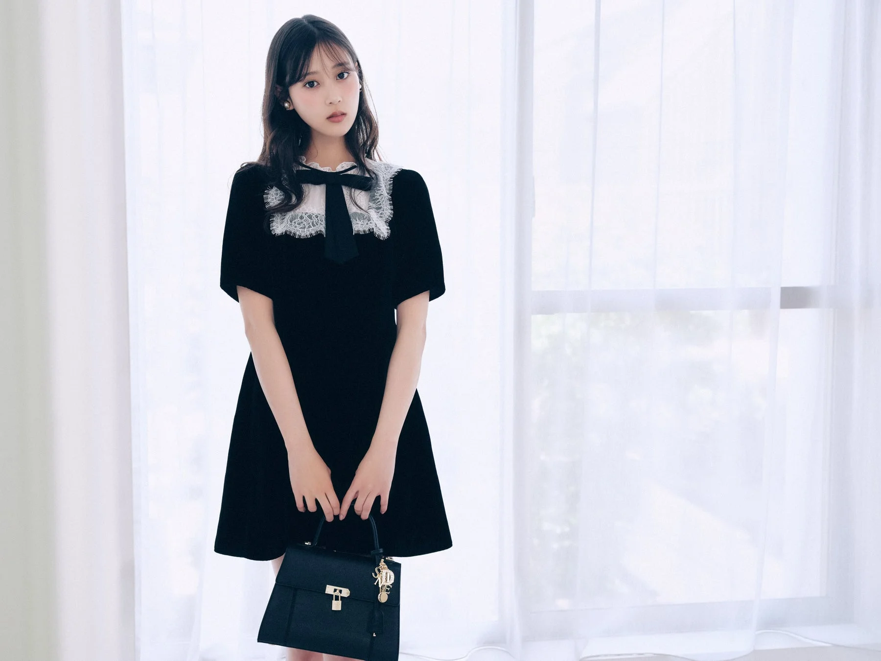 女性が黒いワンピースを着てバッグを持つ