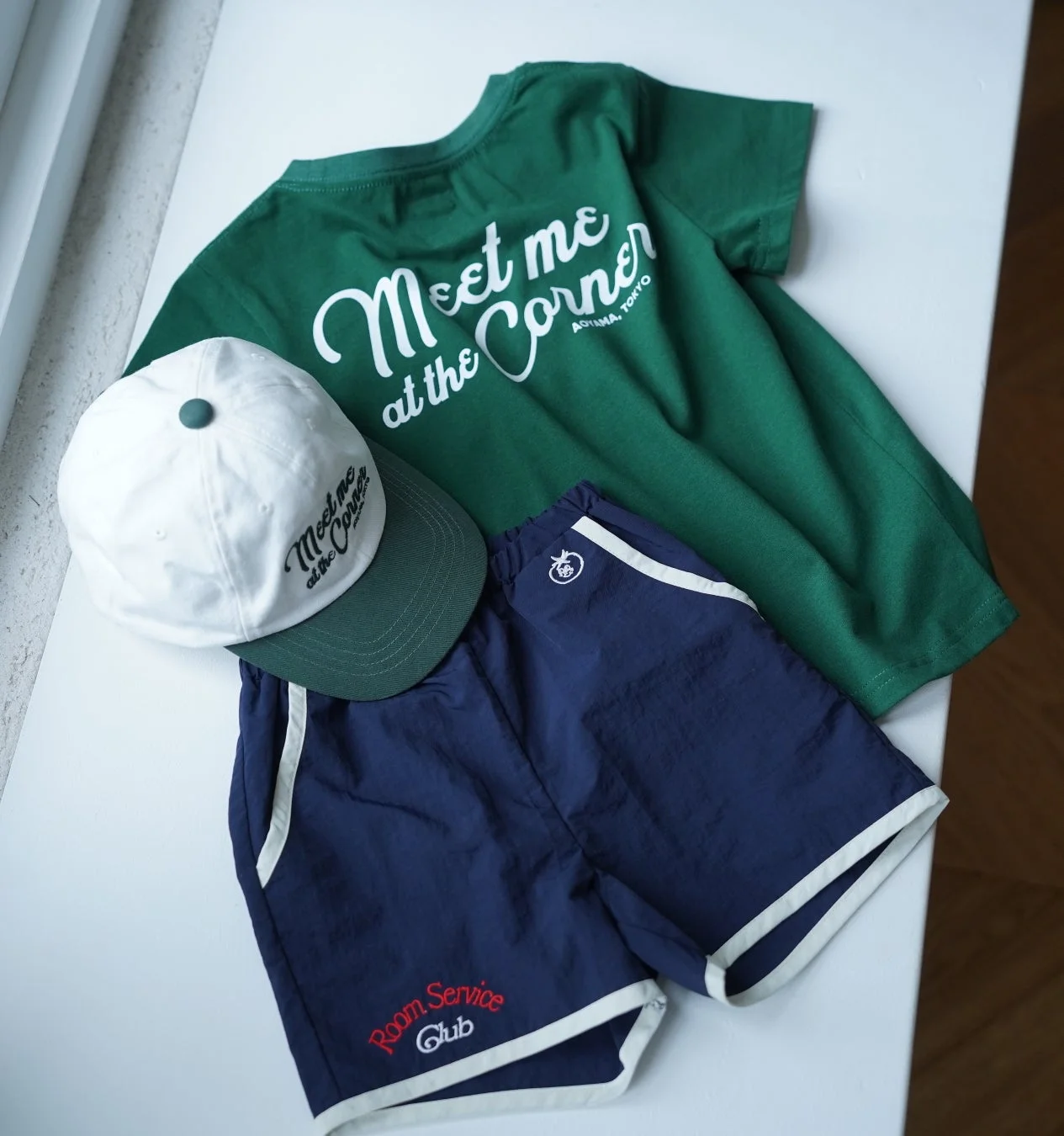 緑のTシャツ、白と緑のキャップ、紺のショートパンツのカジュアルな夏のコーディネート