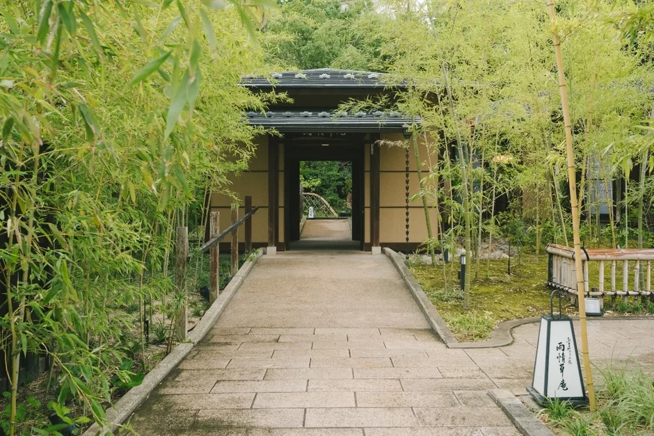 青々とした竹林に囲まれた石畳の小道が、伝統的な和風の門へと続く風景。