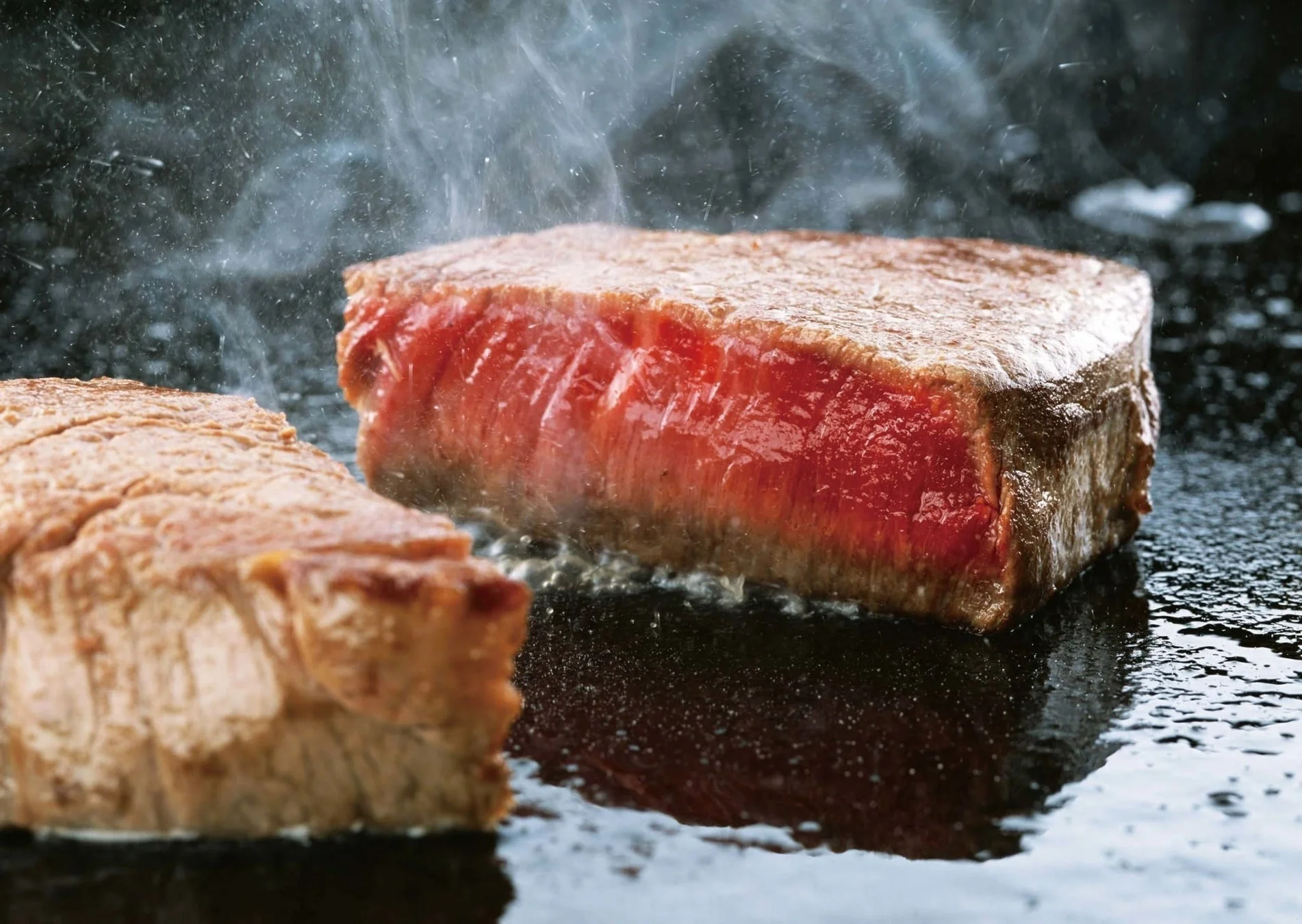 熱い鉄板の上で分厚いステーキ肉が焼かれている様子