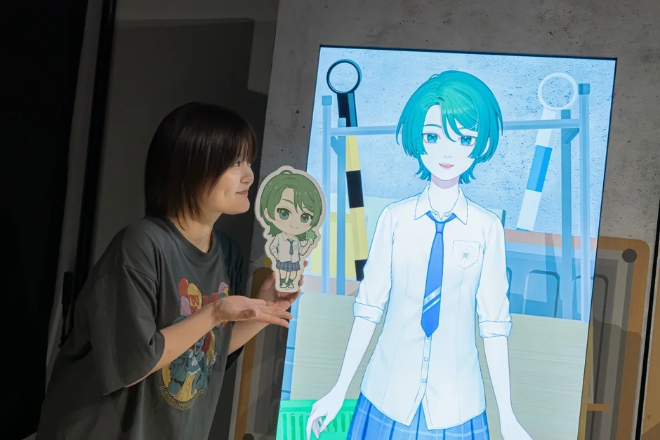 大型スクリーンに映るバーチャルキャラクターとアクリルスタンドを持つ田村好さん