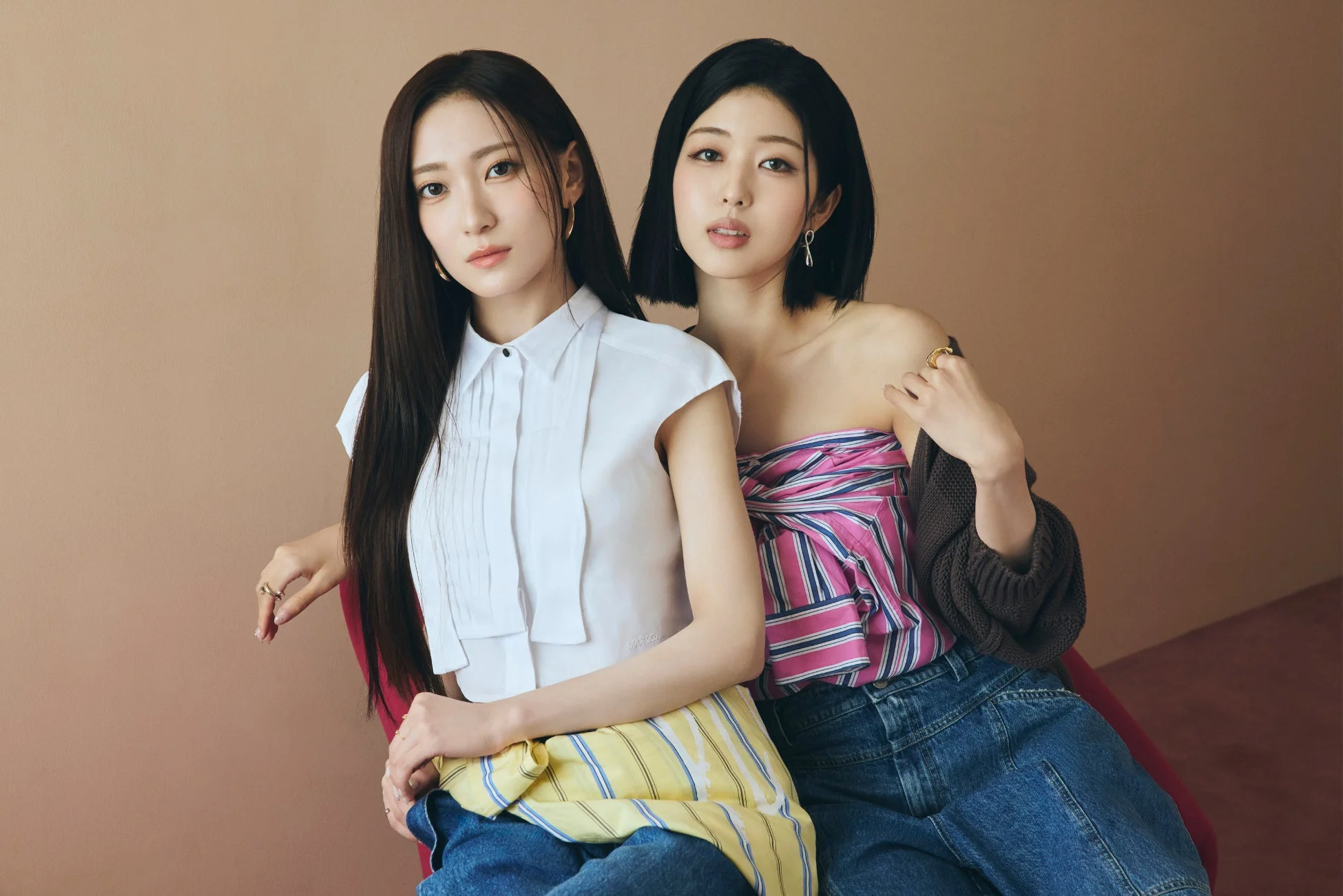 白いシャツとストライプのトップスを着た二人の女性が座ってポーズをとっています
