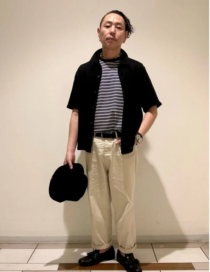 黒の半袖シャツにボーダーTシャツ、ベージュのパンツを合わせた男性
