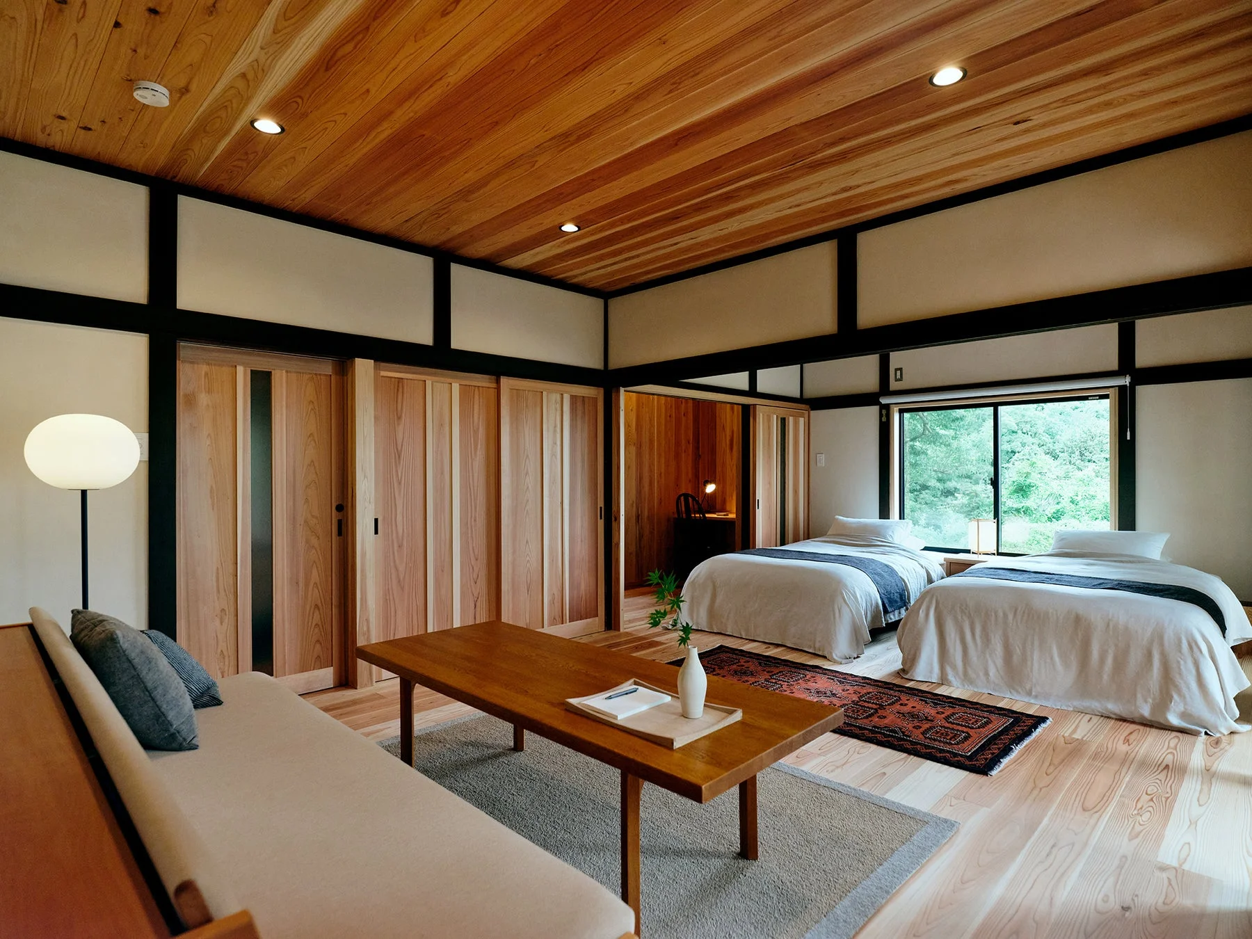 木製の天井と床が特徴的な和モダンの客室。ベッド2台、木製テーブル、ソファが配置され、窓からは豊かな緑が望めます。
