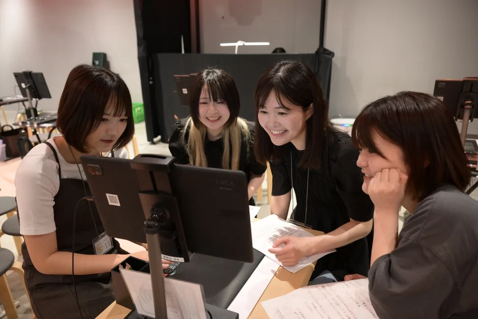 4人の若い女性がテーブルを囲み、タブレットや資料を見ながら笑顔で議論している様子