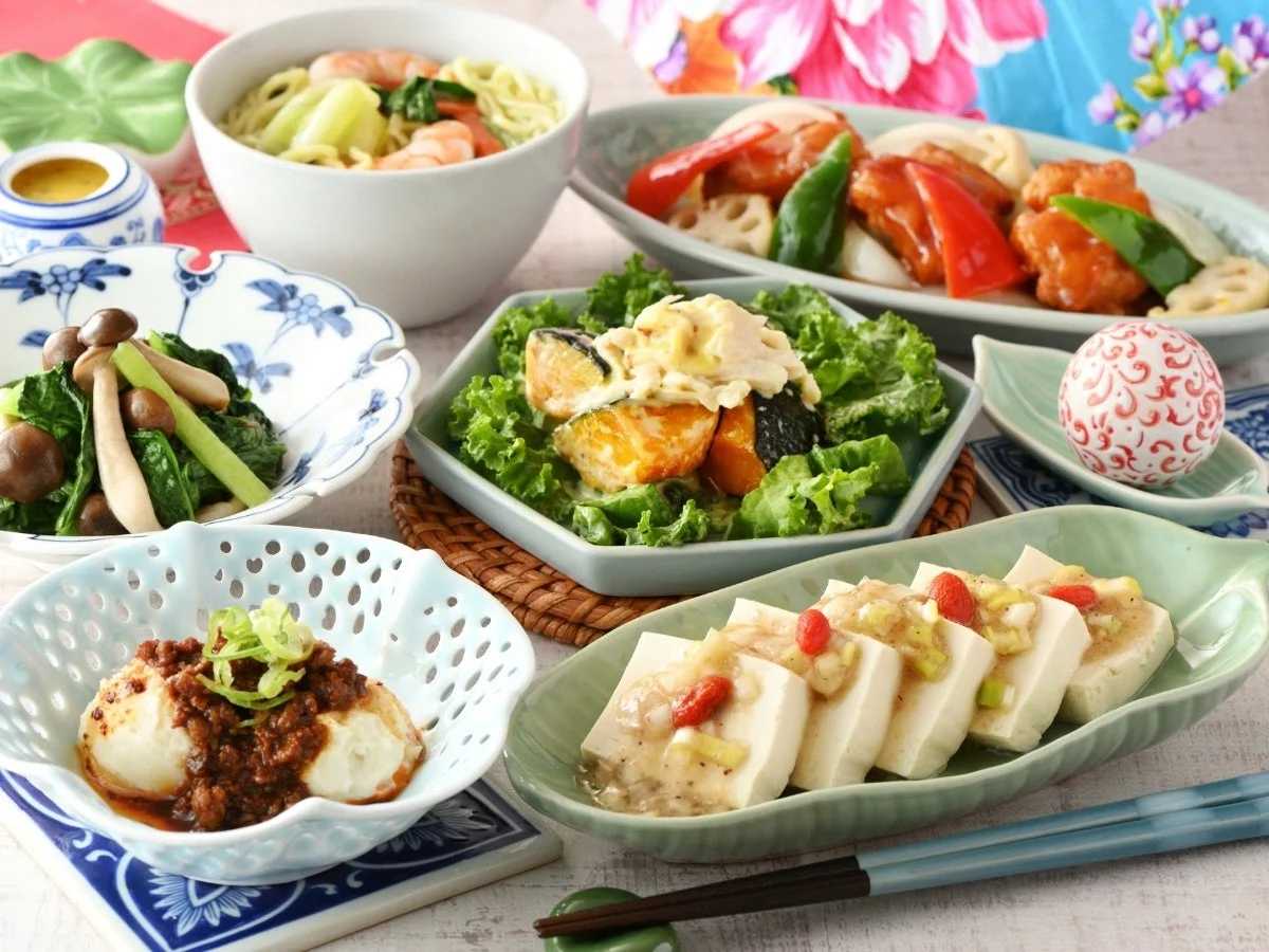 色とりどりの様々なアジア料理が並ぶ食卓。海老と野菜の麺、豆腐料理、甘酢あんかけ、かぼちゃサラダなど、ヘルシーでバランスの取れた食事が豊富に盛り付けられています。見た目も鮮やかで食欲をそそる料理の数々です。