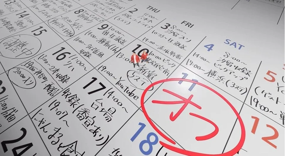 手書きのスケジュールが詳細に書き込まれたカレンダー。日付や時間、イベント名が記され、10日の上にはミニチュアフィギュアが2体、11日には赤い丸と「オウ」の文字がある。収録や配信など日々の予定が確認できる。