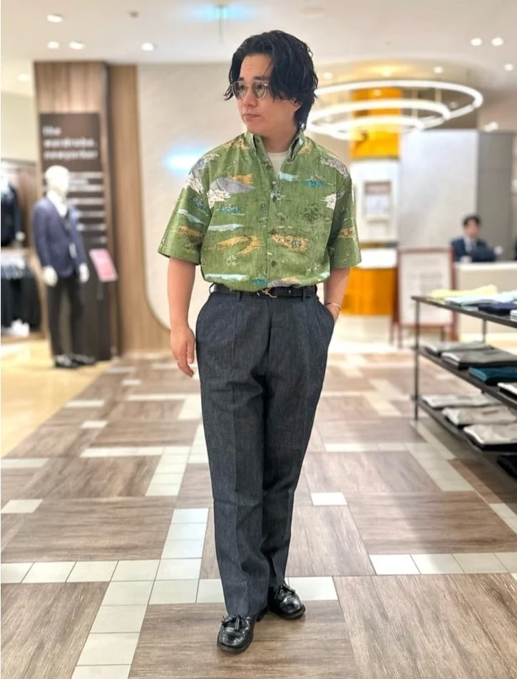 緑色の柄シャツとダークカラーのトラウザーズを着用した男性