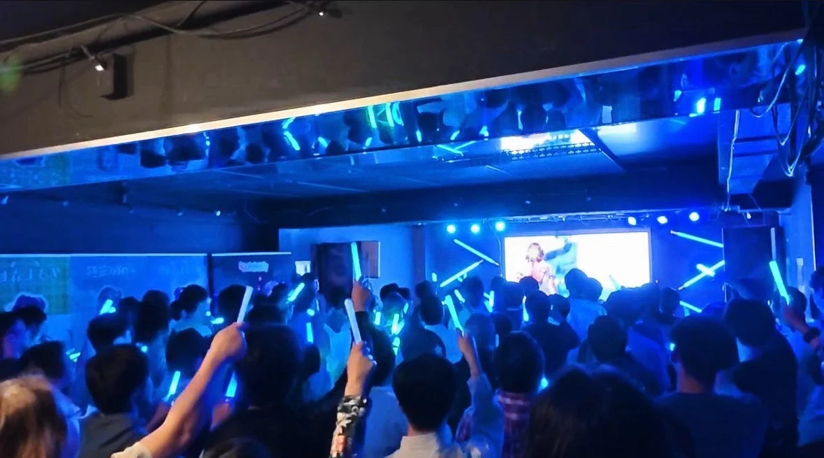 青い光に包まれた会場で、多くの観客が青いペンライトを掲げ、ステージ上のパフォーマンスを楽しんでいるライブイベントの様子です。