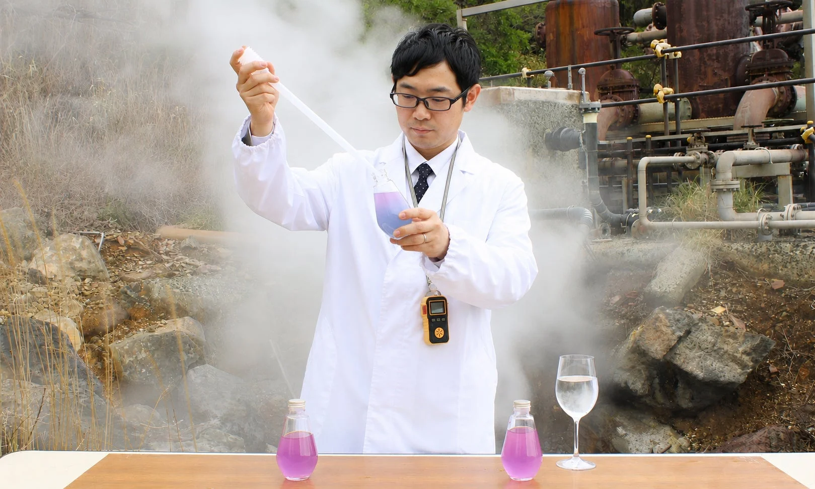 白衣を着た男性が湯気が立ち上る屋外で化学実験を行っています