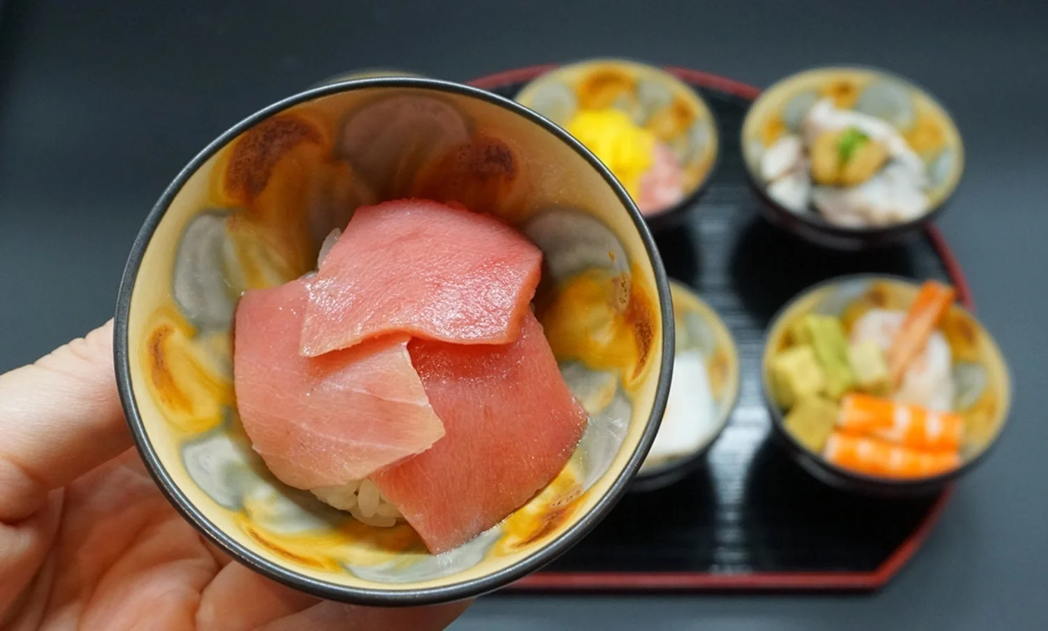 手で持たれたミニ丼と奥に並ぶ様々なミニ丼