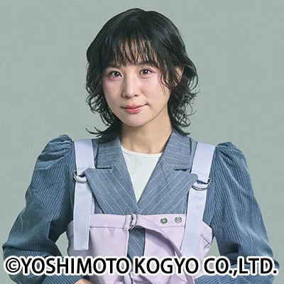 ショートヘアの若い女性が、グレーのストライプジャケットとラベンダー色のエプロン風トップスを着用し、カメラに向かって優しく微笑んでいるポートレート写真。
