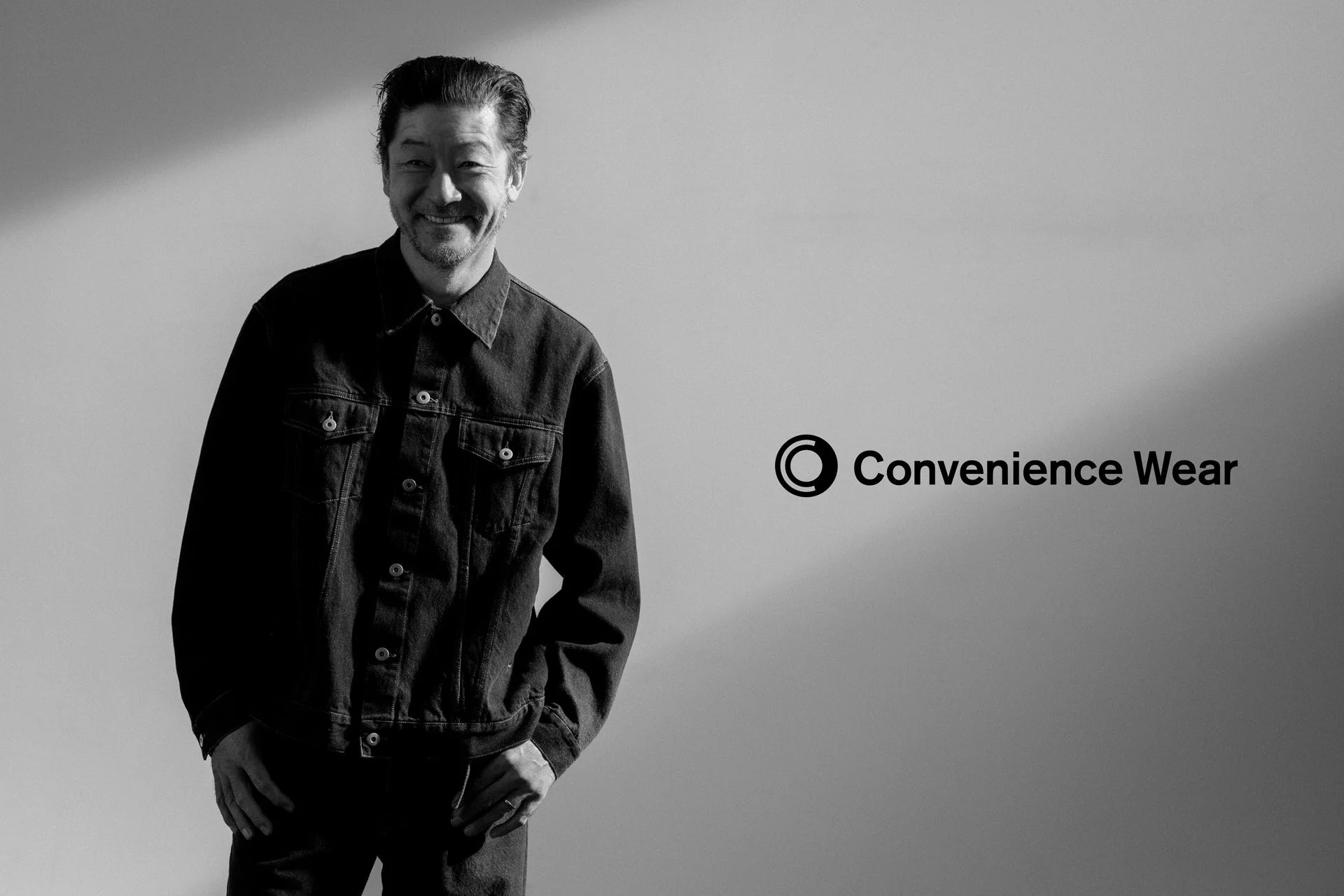 デニムジャケットを着用し、笑顔を見せる男性の白黒ポートレート。右側には「Convenience Wear」のロゴが配置されている。