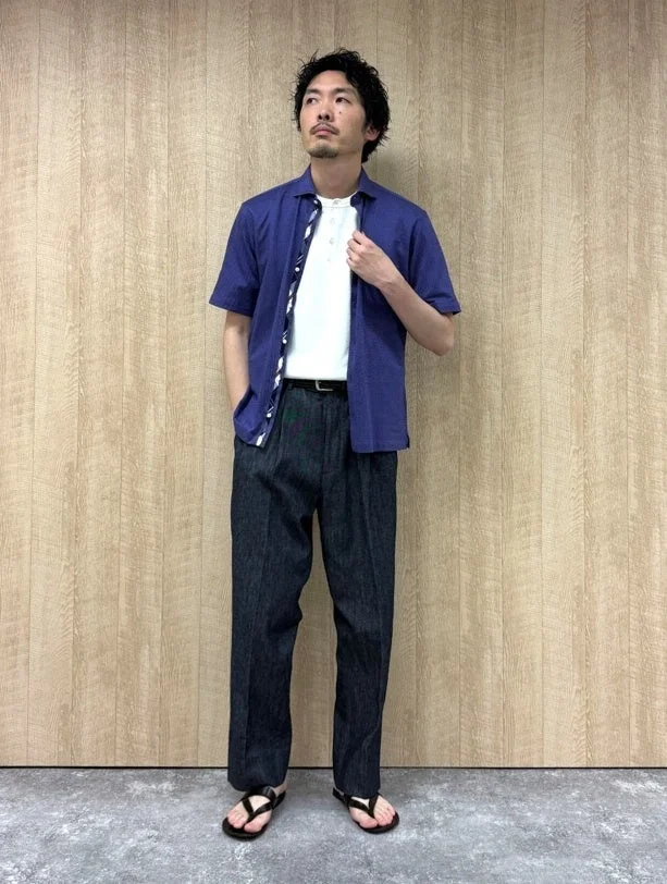 ネイビーの開襟シャツを白のヘンリーネックTシャツの上に羽織り、ダークカラーのワイドパンツと黒いサンダルを合わせた男性