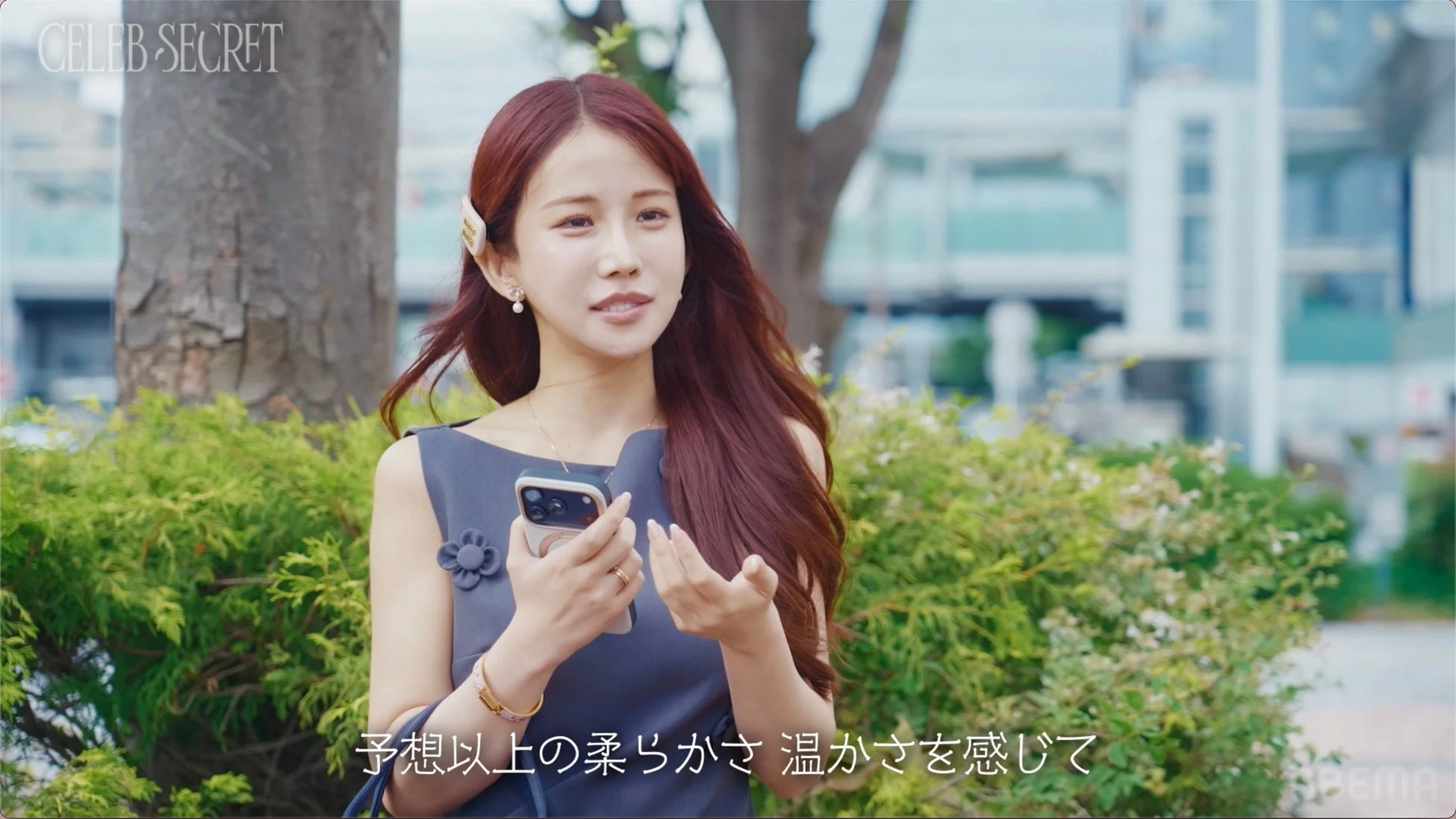 屋外でスマートフォンを持つ、赤みがかったロングヘアの若い女性のポートレート。