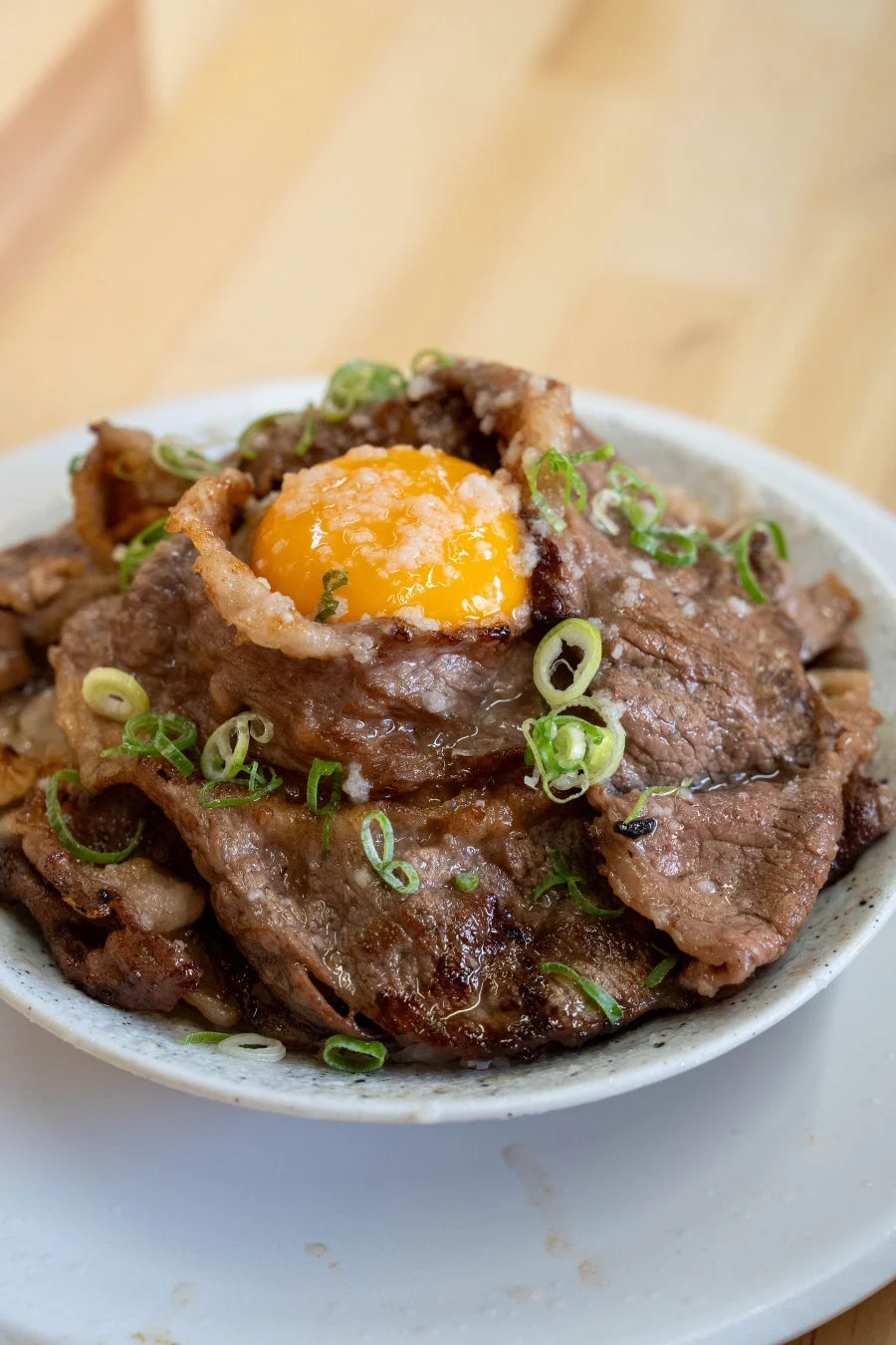 薄切り牛肉を盛り付けた丼で、中央には鮮やかな黄色の卵黄が乗り、刻んだネギが散らされています。食欲をそそる一品です。