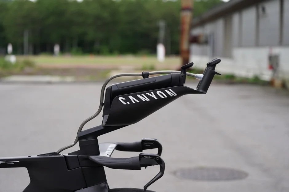 黒いCANYONブランドのタイムトライアルバイクのハンドル部分をクローズアップした画像。エアロバーやブレーキレバーなどの詳細なコンポーネントが写っており、屋外の舗装路が背景となっています。
