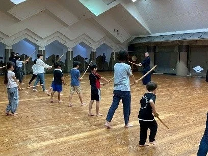 子供たちが木刀や棒のようなものを持って武道の稽古に励んでいる様子