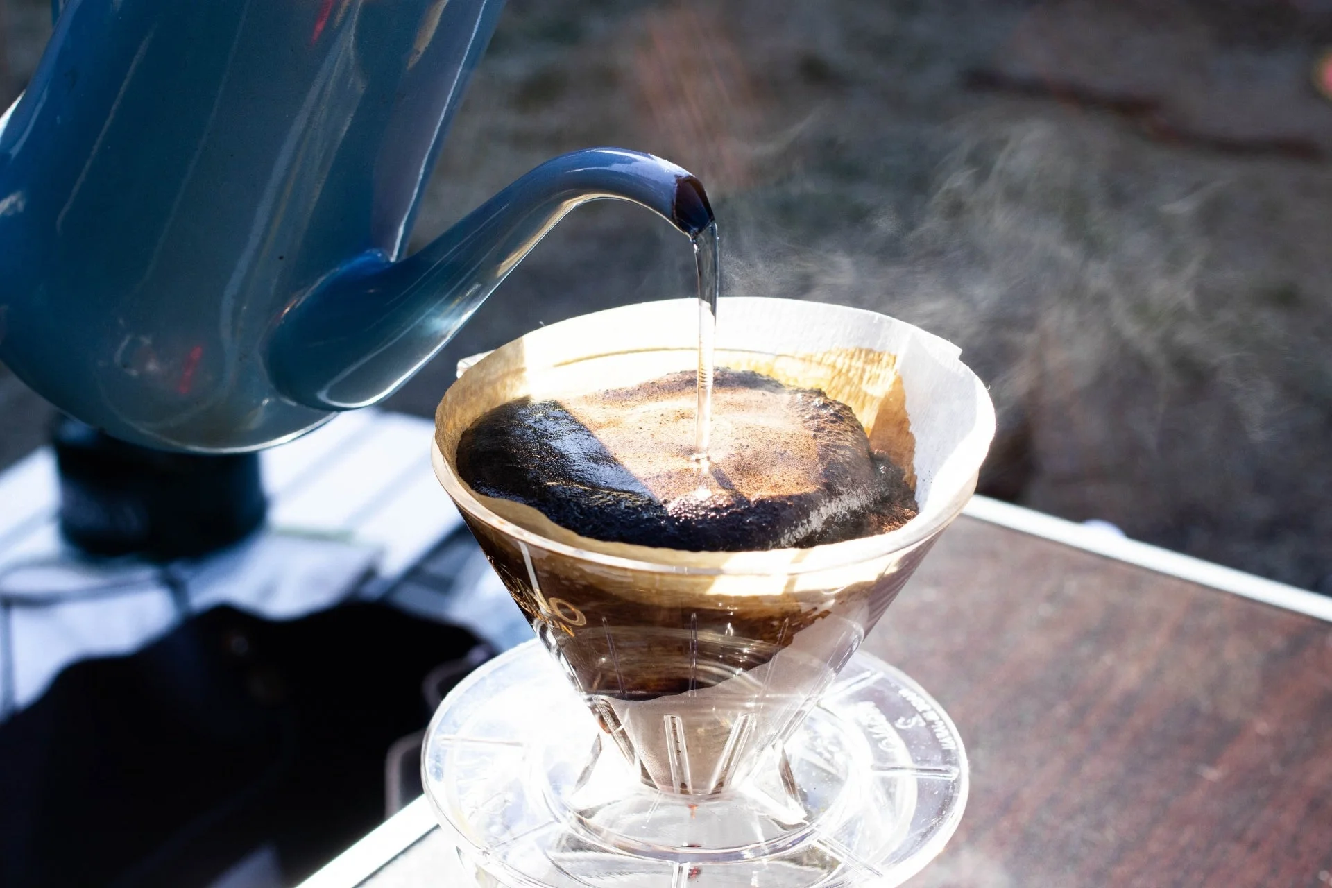 ケトルからコーヒー粉にお湯を注ぎ、ドリップコーヒーを淹れている瞬間を捉えた写真です。湯気が立ち上り、淹れたてのコーヒーの香りが漂ってきそうな、リラックスした雰囲気が伝わります。