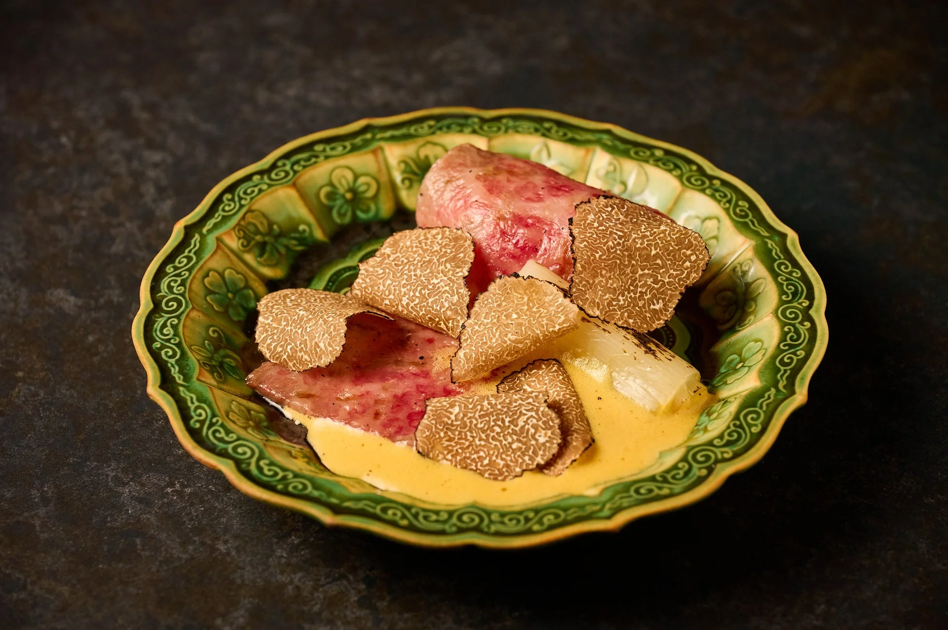 美しい緑の皿に盛り付けられた、肉と濃厚なソース、そして惜しみなくスライスされたトリュフが特徴の高級感あふれる料理。洗練された盛り付けが食欲をそそります。