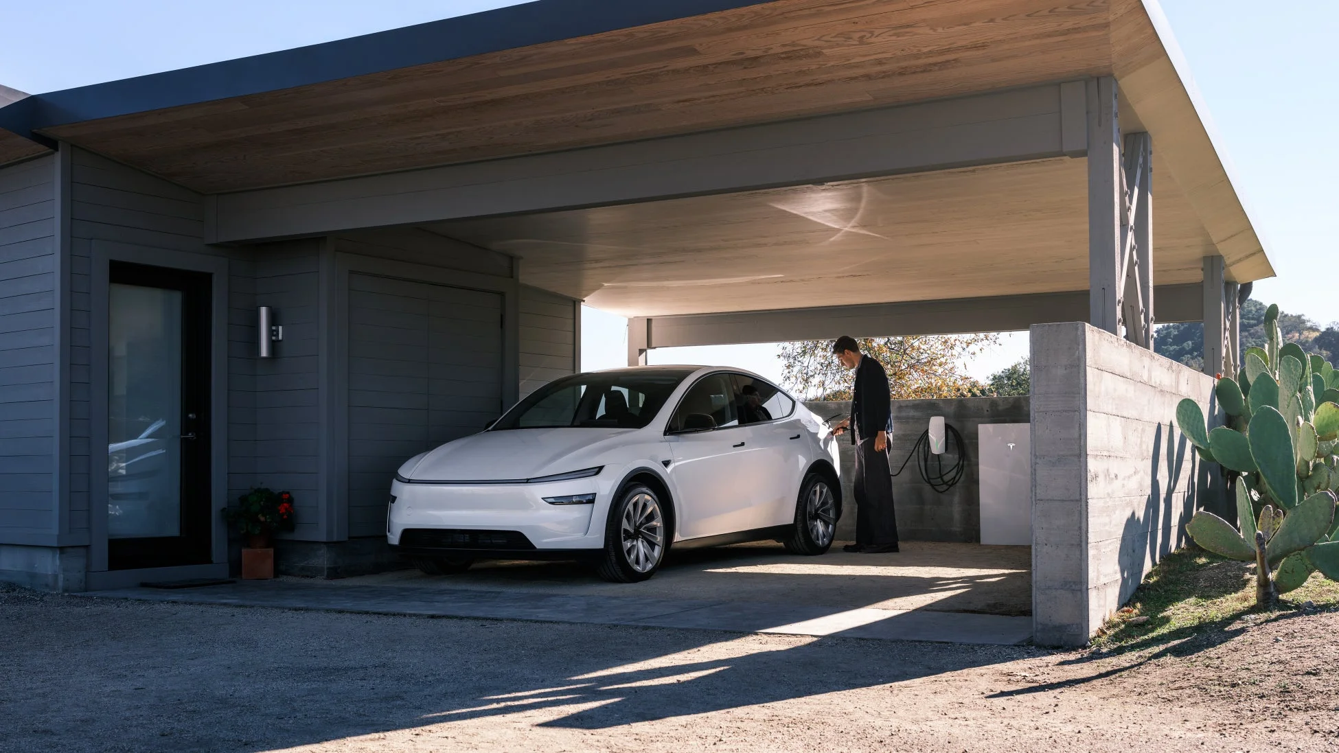 モダンな家屋のカーポートで充電中の白いテスラ Model Y
