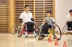 室内でスポーツ用車椅子に乗った大人と子供が、コーンを置いて車椅子操作のトレーニングをしている場面です。