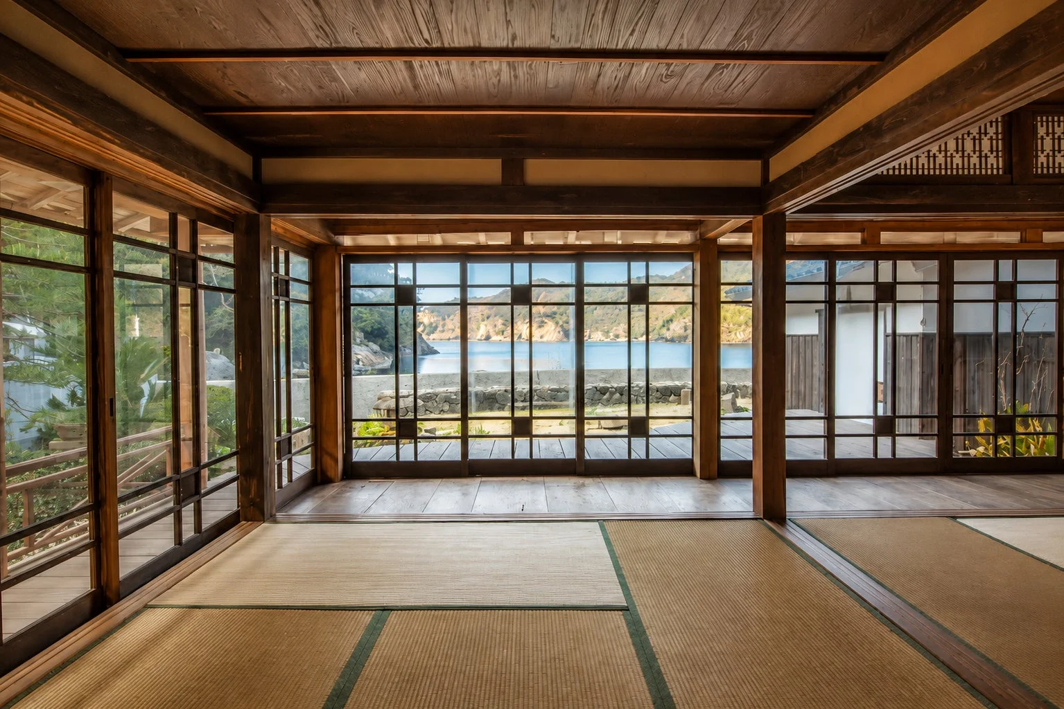 畳が敷かれた伝統的な和室から、大きな窓越しに穏やかな海と山々が広がる絶景を望む