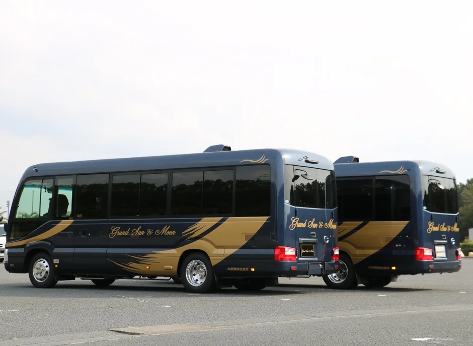 青とゴールドのツートンカラーの観光バスが2台、駐車場に並んで停まっています。