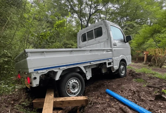 森の中のぬかるんだ道に駐車された白い軽トラック