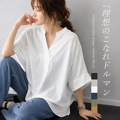 白いドルマンスリーブのスキッパーブラウスと青いパンツを着用した女性が、リラックスしたポーズで座っています。理想のこなれ感を演出するポリエステルローン素材のブラウスで、大人カジュアルな着こなしを提案しています。