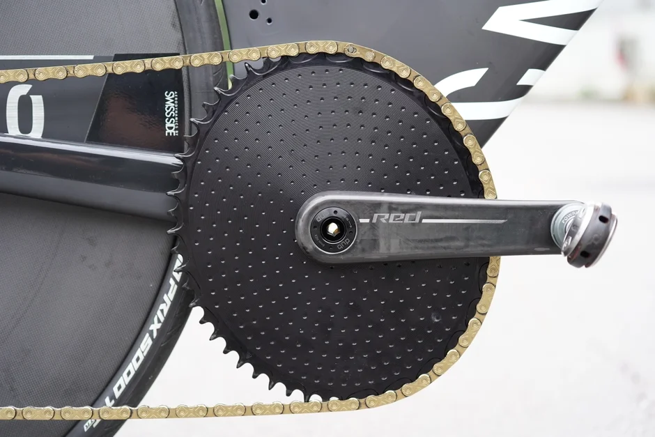 高性能な競技用自転車のドライブトレイン部分をクローズアップ。SRAM REDクランク、Quarqパワーメーター、エアロディスクチェーンリング、ゴールドチェーンが特徴的。精密なコンポーネントが強調されている。