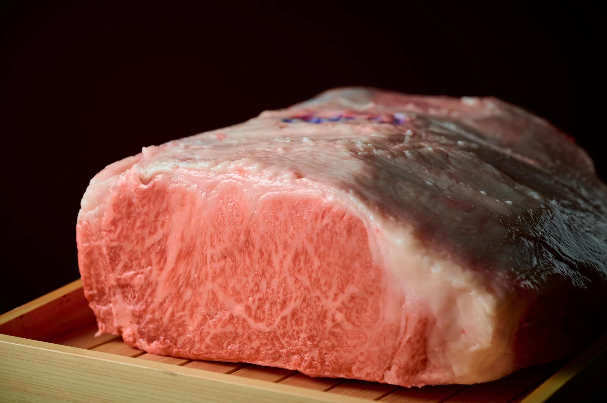 木製のトレイに置かれた、きめ細やかな霜降りが美しい高級和牛肉の塊が写っています。鮮やかな赤身と白い脂身のコントラストが特徴的です。