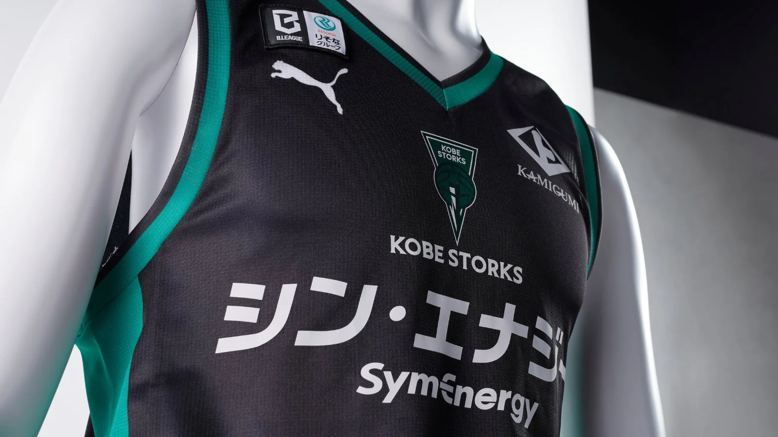 マネキンが着用する黒とエメラルドグリーンのバスケットボールユニフォーム。B.LEAGUE、KOBE STORKS、PUMAのロゴに加え、スポンサー名が鮮明に見える。