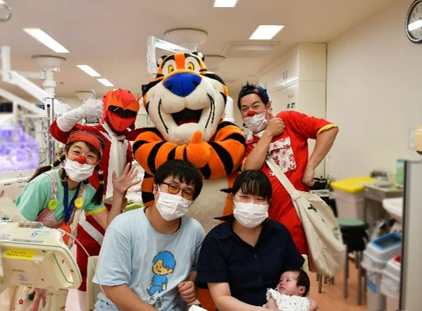 病棟で赤ちゃんを囲むトニー・ザ・タイガーとクリニクラウン