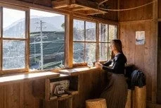 木製の温かい雰囲気の部屋から外の山々と自然の景色を眺める女性