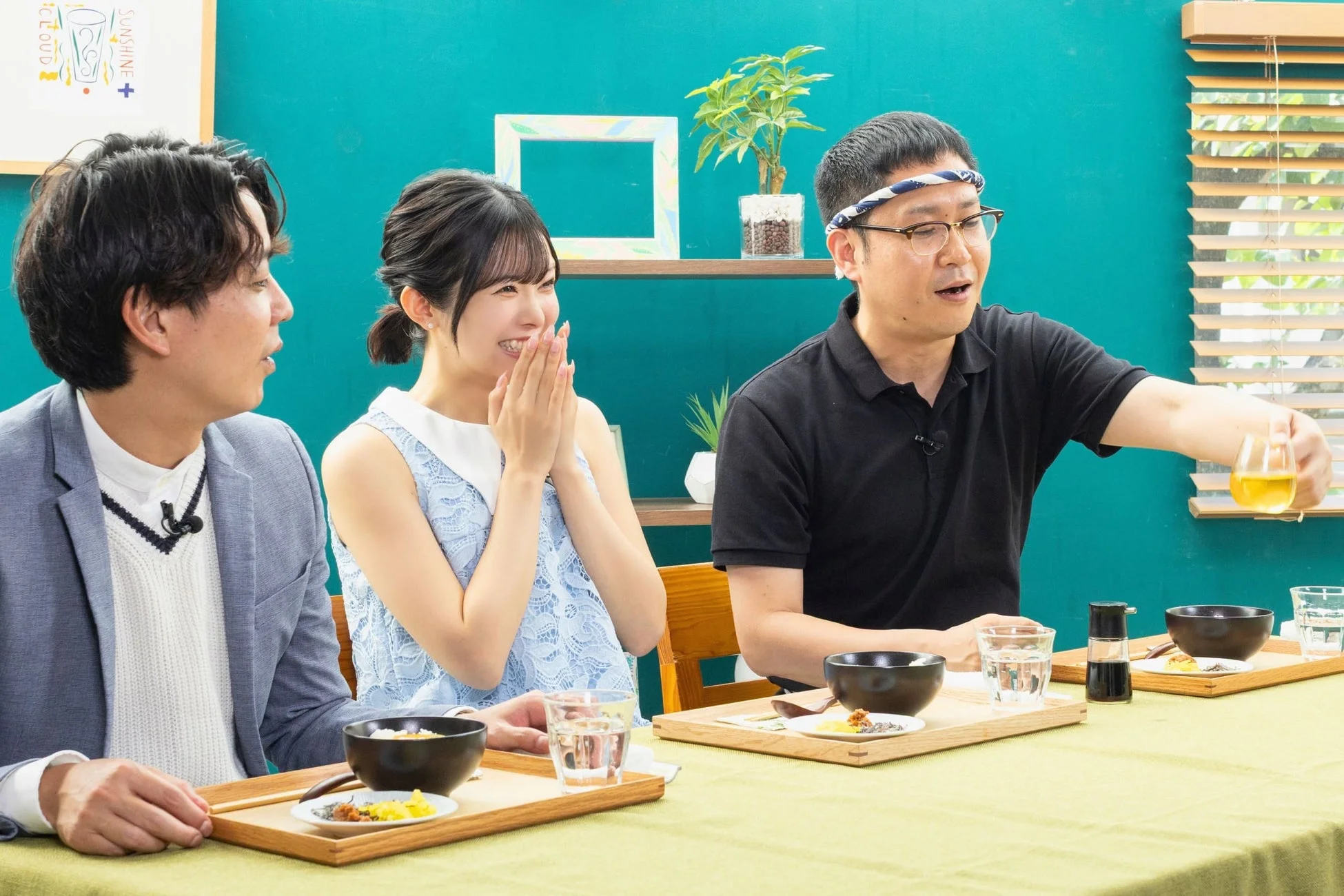 明るいスタジオのような場所で、男女3人が食事をしながら談笑している様子