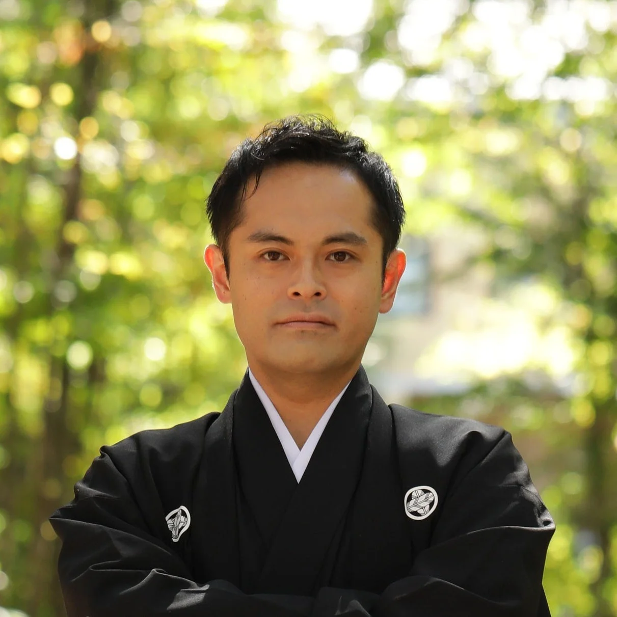 緑豊かな屋外を背景に、紋付羽織袴を着用した日本人男性がカメラを見つめているポートレート