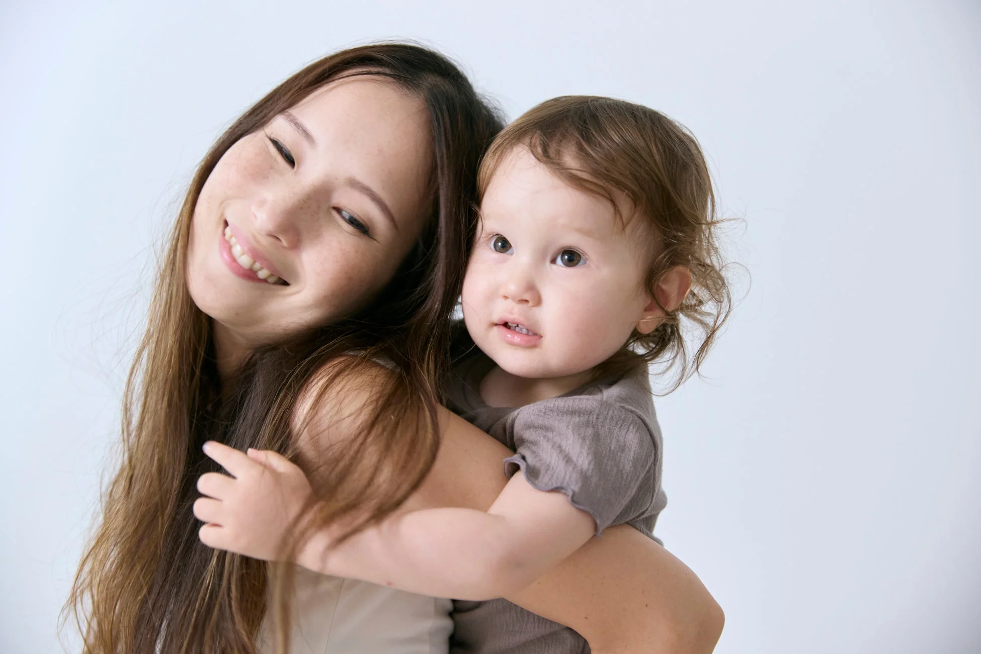 母親が赤ちゃんを抱きしめ、幸せそうな笑顔を見せています。赤ちゃんは何かを見つめているようで、温かい親子の絆が感じられる一枚です。