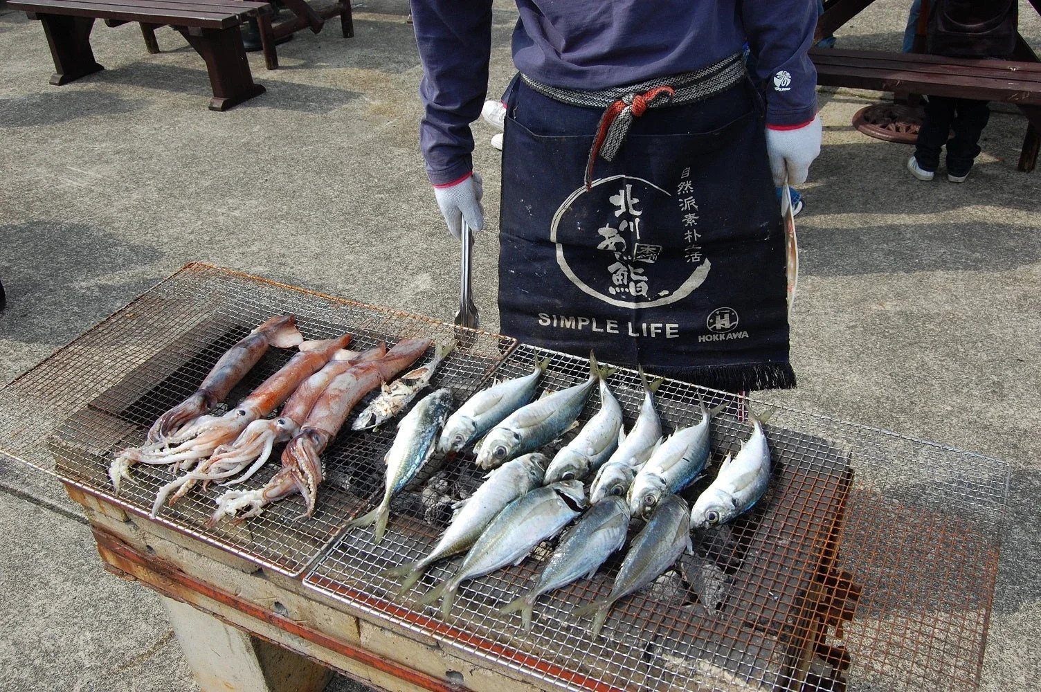屋外で炭火焼きグリルを使ってイカとたくさんの魚を焼いている