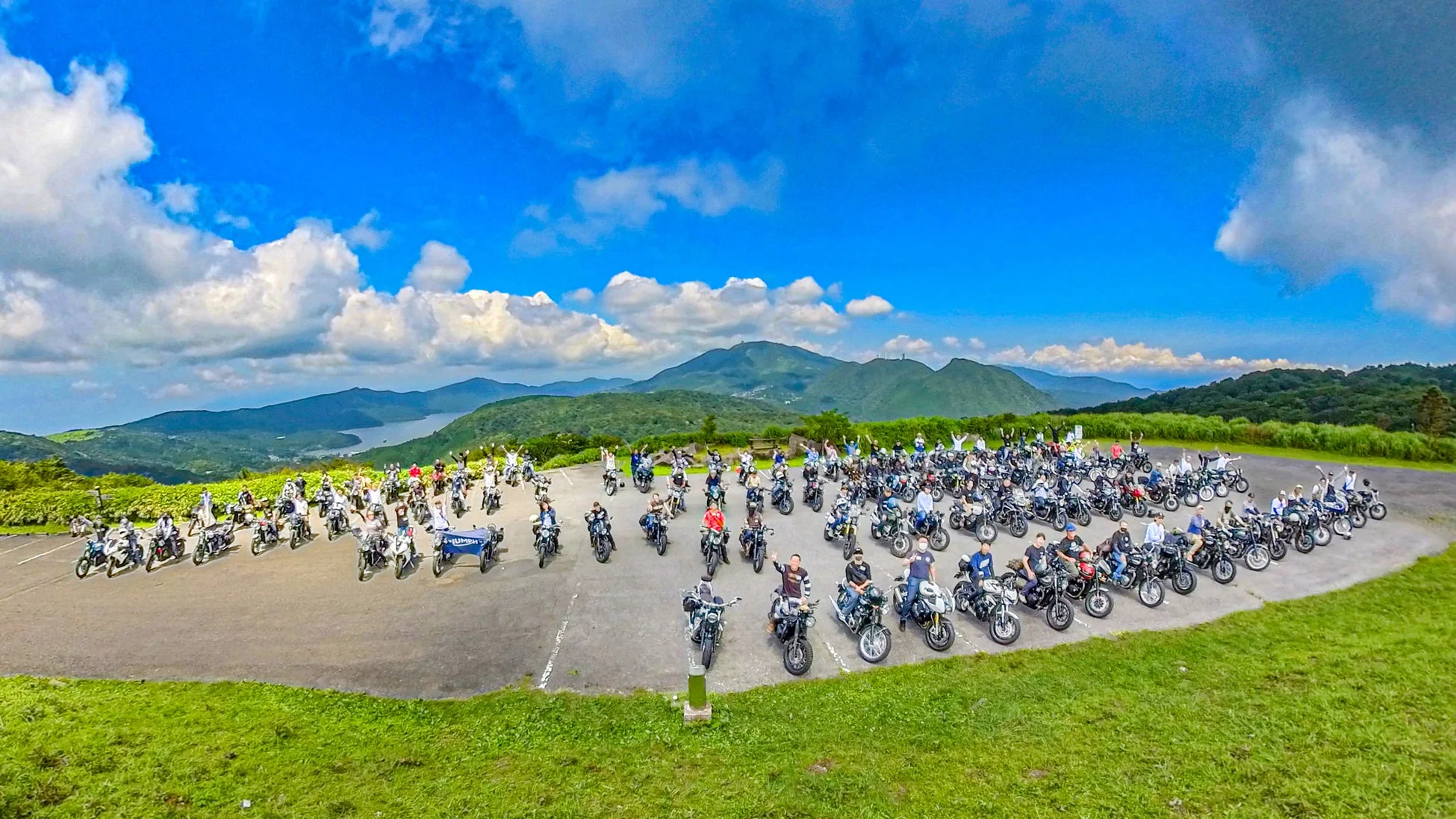 多くのオートバイとライダーたちが景色の良い場所で集合写真を撮っている様子