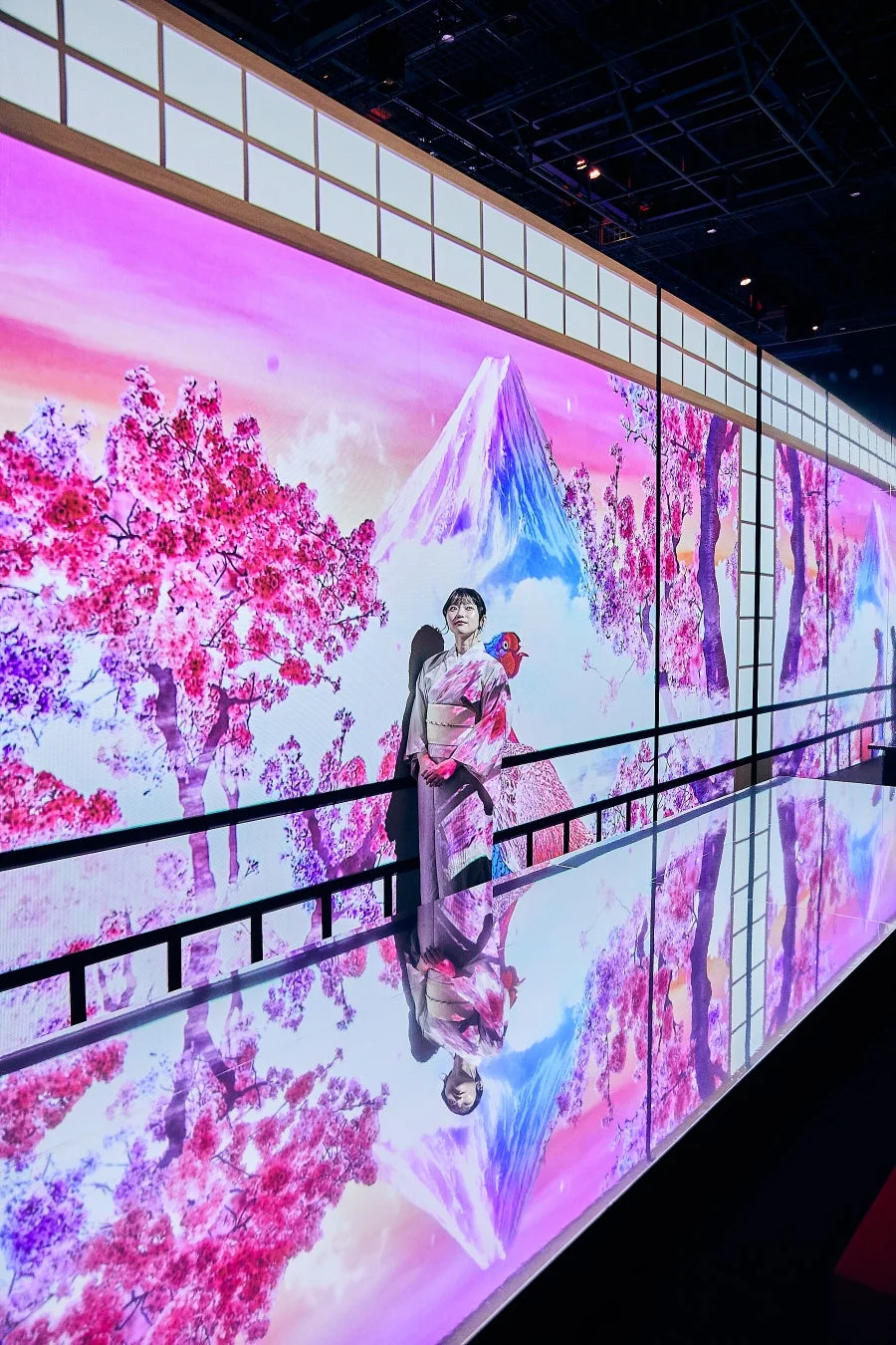 着物を着た女性が、富士山と満開の桜が描かれた鮮やかなプロジェクションマッピングの前に立っています。床にはその美しい光景が反射し、幻想的な空間を演出しています。